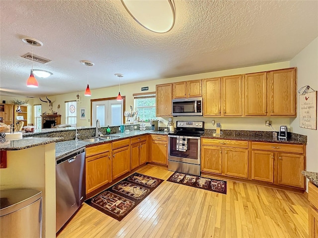 kitchen with stainless steel appliances, pendant lighting, light wood-type flooring, and a textured ceiling