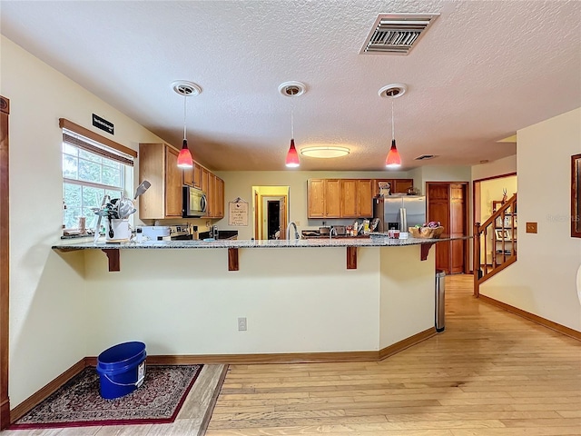 kitchen featuring stainless steel appliances, hanging light fixtures, a breakfast bar, and light wood-type flooring