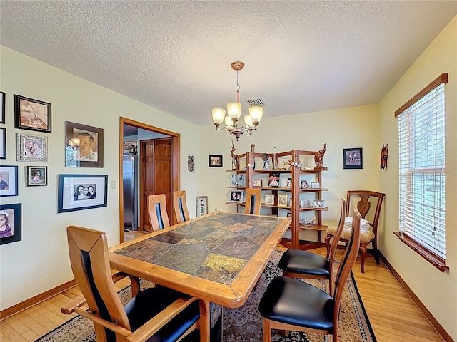 dining room featuring an inviting chandelier, a textured ceiling, and light wood-type flooring