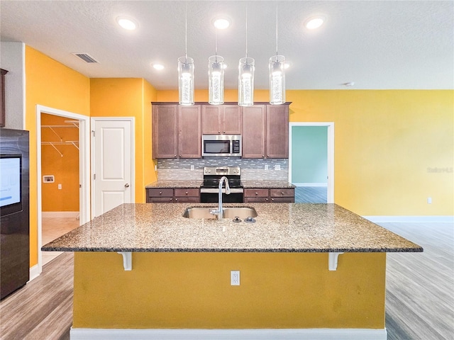 kitchen featuring light stone counters, stainless steel appliances, light wood-type flooring, and a kitchen bar