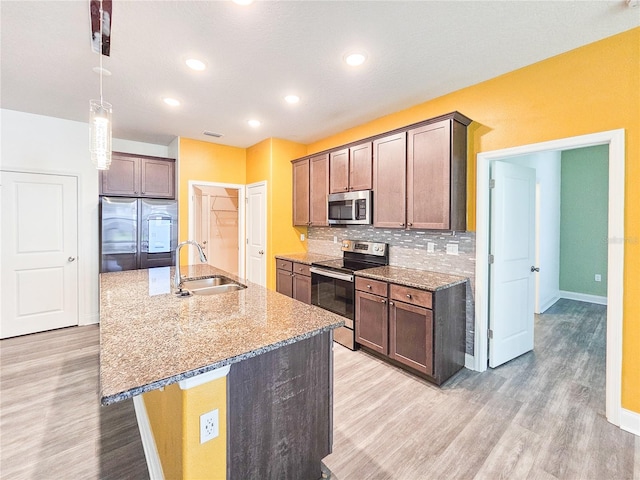 kitchen with a kitchen island with sink, light wood-type flooring, light stone counters, sink, and appliances with stainless steel finishes