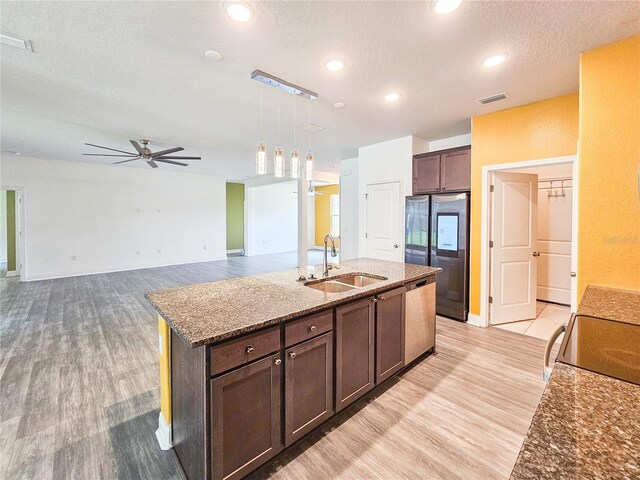 kitchen featuring hanging light fixtures, sink, a center island with sink, dark stone countertops, and light hardwood / wood-style floors