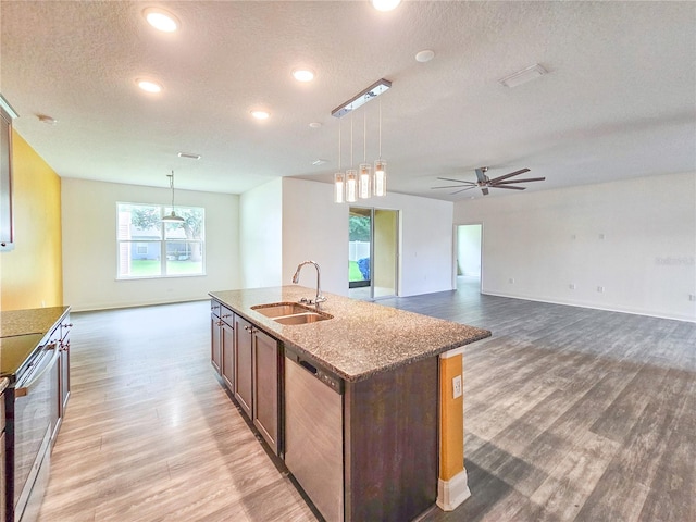 kitchen with an island with sink, sink, a textured ceiling, decorative light fixtures, and appliances with stainless steel finishes