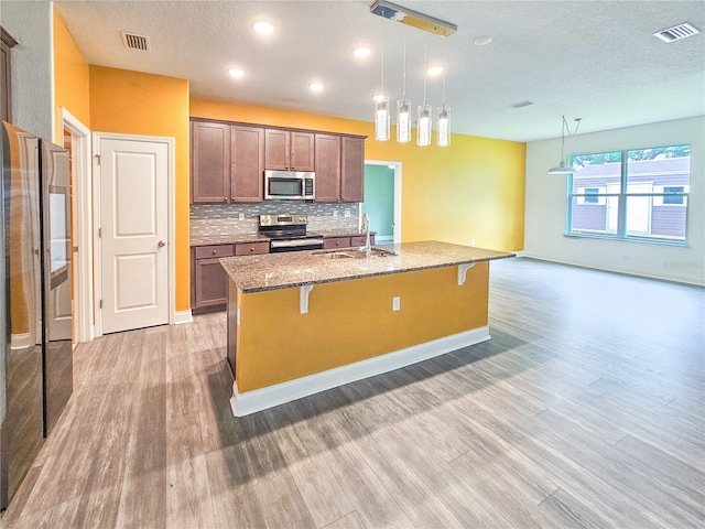 kitchen featuring light hardwood / wood-style floors, sink, hanging light fixtures, appliances with stainless steel finishes, and an island with sink