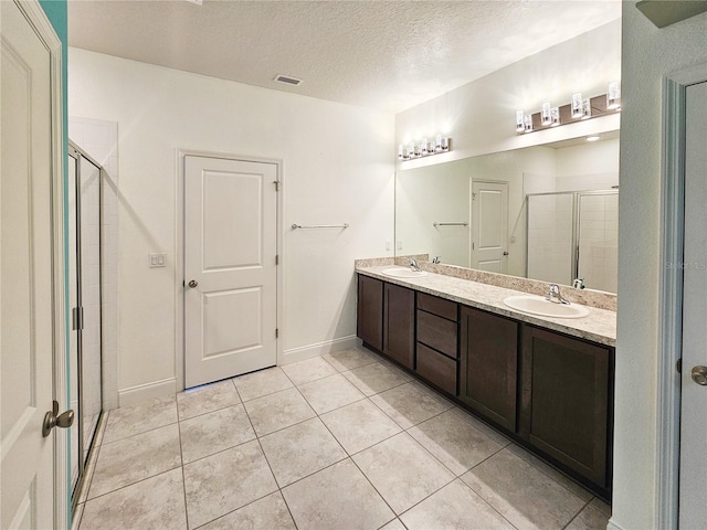 bathroom with tile patterned flooring, a shower with door, vanity, and a textured ceiling