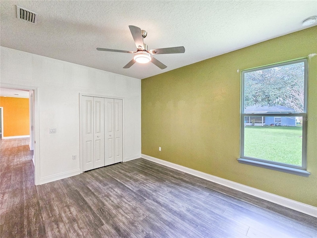 unfurnished bedroom with a textured ceiling, ceiling fan, a closet, and dark hardwood / wood-style flooring