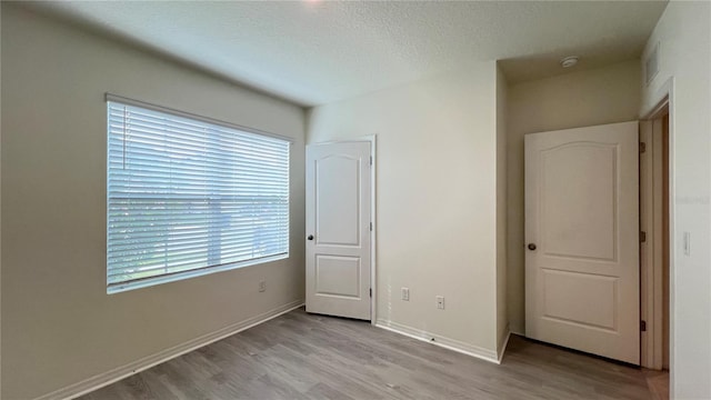 unfurnished bedroom featuring a textured ceiling, multiple windows, and light wood-type flooring