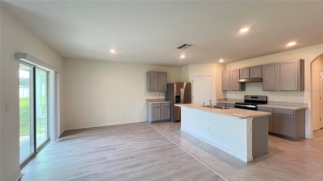 kitchen featuring gray cabinetry, a textured ceiling, light hardwood / wood-style floors, stainless steel appliances, and a center island with sink