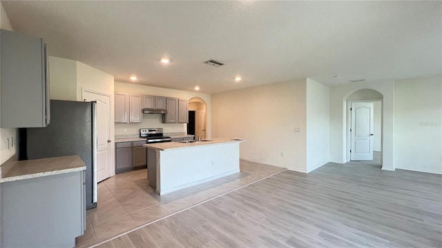 kitchen with stainless steel appliances, a center island with sink, sink, light wood-type flooring, and gray cabinets