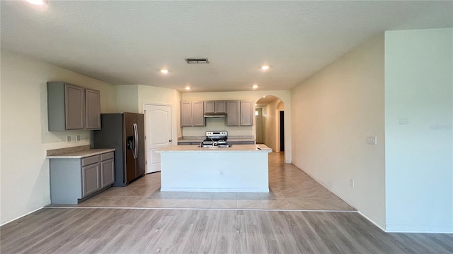 kitchen with gray cabinets, a kitchen island with sink, stainless steel appliances, and light wood-type flooring