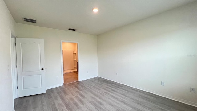 unfurnished bedroom with ensuite bathroom and light wood-type flooring