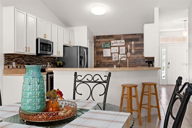 kitchen featuring light tile patterned floors, kitchen peninsula, white cabinetry, appliances with stainless steel finishes, and decorative backsplash