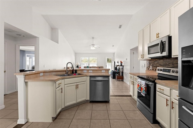 kitchen with stainless steel appliances, sink, vaulted ceiling, a center island with sink, and light tile patterned floors