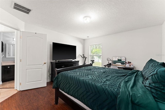 bedroom featuring hardwood / wood-style flooring, ensuite bath, and a textured ceiling