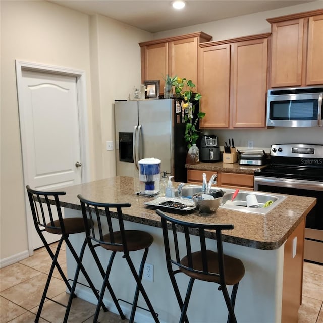 kitchen featuring appliances with stainless steel finishes, a center island with sink, a kitchen bar, and light tile patterned floors