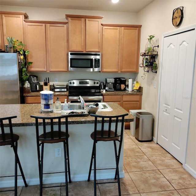 kitchen featuring light brown cabinetry, an island with sink, a breakfast bar area, stainless steel appliances, and light tile patterned floors