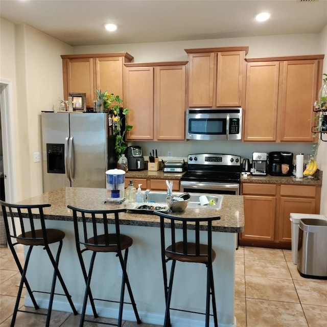 kitchen with stainless steel appliances, a center island with sink, a breakfast bar, light tile patterned floors, and light stone counters