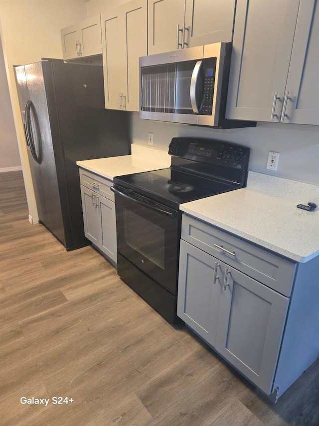 kitchen with gray cabinetry, light hardwood / wood-style flooring, and black appliances