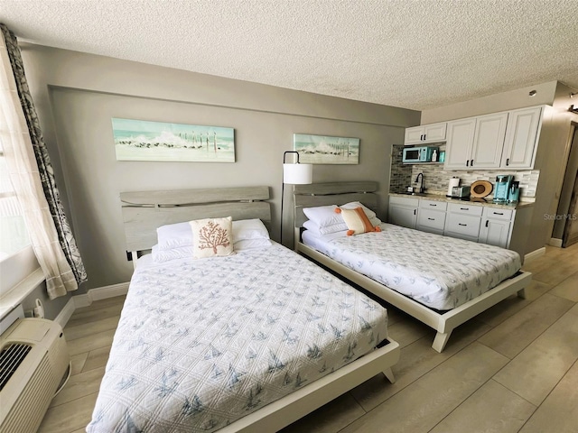 bedroom featuring light hardwood / wood-style floors, an AC wall unit, a textured ceiling, and sink