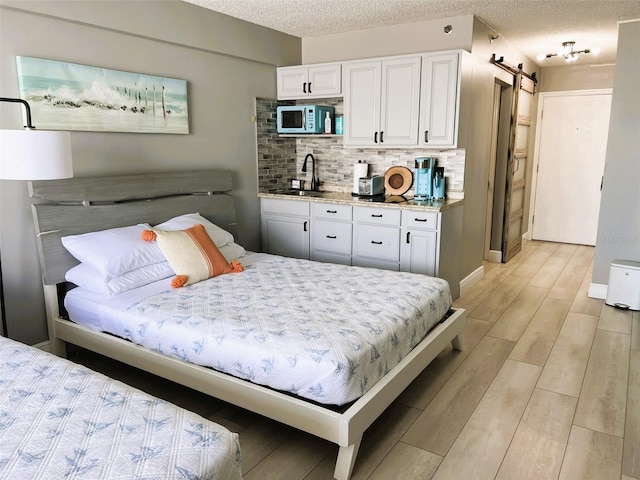 bedroom featuring sink, a textured ceiling, light hardwood / wood-style flooring, and a barn door