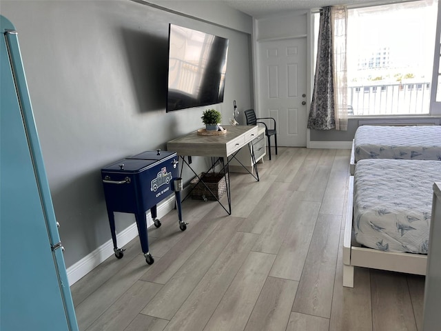 bedroom with light hardwood / wood-style floors and stainless steel fridge