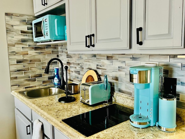 kitchen featuring light stone countertops, sink, decorative backsplash, and white cabinetry