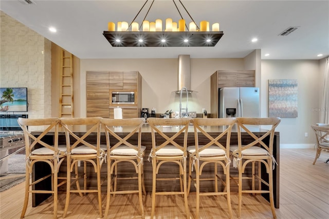 kitchen featuring a kitchen breakfast bar, light hardwood / wood-style flooring, stainless steel appliances, range hood, and decorative light fixtures