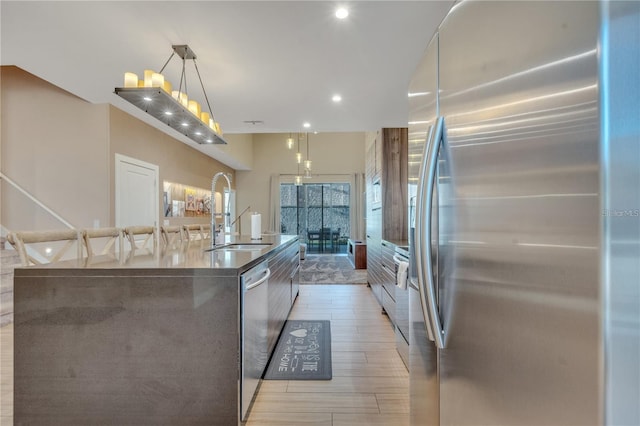 kitchen featuring a spacious island, sink, decorative light fixtures, light wood-type flooring, and appliances with stainless steel finishes