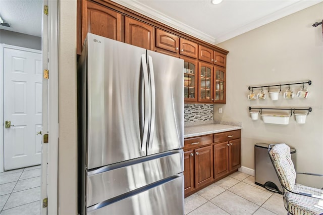 kitchen featuring crown molding, decorative backsplash, light tile patterned floors, and stainless steel refrigerator