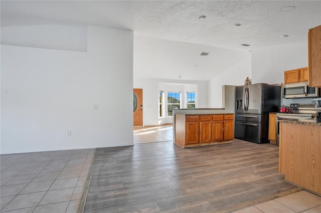 kitchen with lofted ceiling, hardwood / wood-style floors, kitchen peninsula, appliances with stainless steel finishes, and a textured ceiling