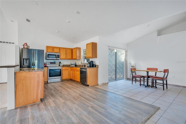 kitchen featuring appliances with stainless steel finishes, light stone counters, high vaulted ceiling, and light wood-type flooring