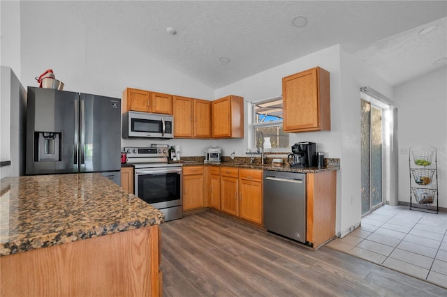 kitchen with a textured ceiling, appliances with stainless steel finishes, vaulted ceiling, and dark hardwood / wood-style floors