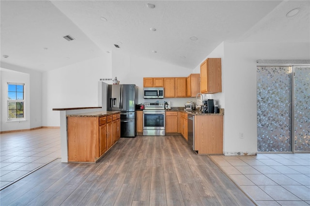 kitchen featuring light hardwood / wood-style flooring, stainless steel appliances, vaulted ceiling, and dark stone counters