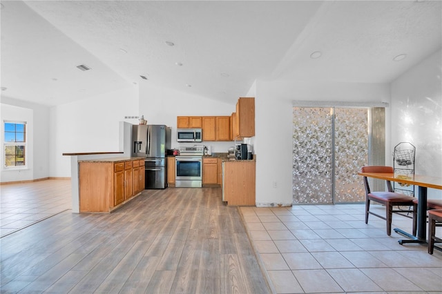 kitchen featuring stone counters, appliances with stainless steel finishes, light wood-type flooring, kitchen peninsula, and lofted ceiling