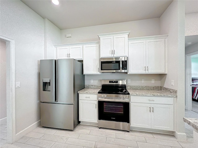 kitchen featuring light stone counters, appliances with stainless steel finishes, light tile patterned floors, and white cabinets