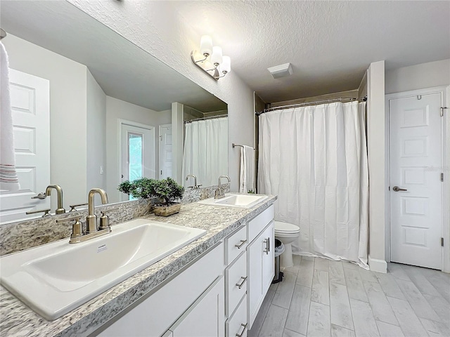 bathroom with hardwood / wood-style flooring, toilet, curtained shower, vanity, and a textured ceiling