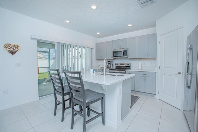 kitchen with appliances with stainless steel finishes, sink, an island with sink, a textured ceiling, and a breakfast bar