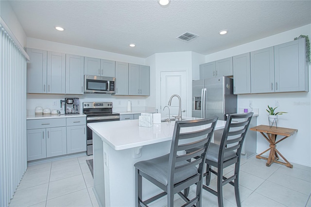 kitchen featuring a center island with sink, a breakfast bar area, a textured ceiling, light tile patterned flooring, and stainless steel appliances