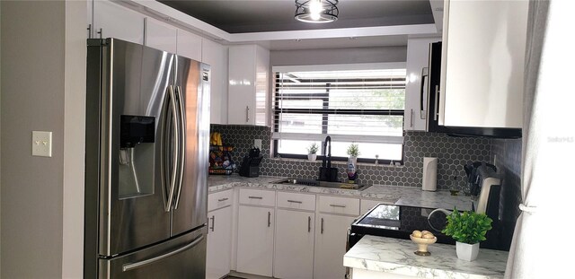 kitchen featuring sink, stainless steel fridge, stove, white cabinets, and decorative backsplash