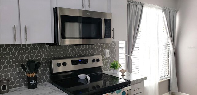 kitchen with appliances with stainless steel finishes, white cabinets, and backsplash