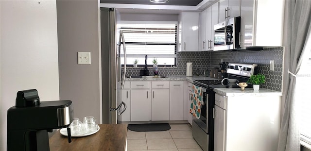 kitchen with stainless steel appliances, sink, light tile patterned flooring, white cabinetry, and tasteful backsplash