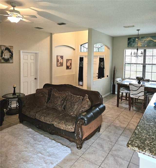 living room featuring a textured ceiling, ceiling fan with notable chandelier, and light tile patterned floors