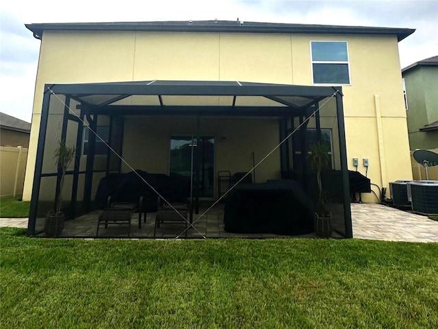 back of house featuring a lawn, glass enclosure, central AC unit, and a patio area