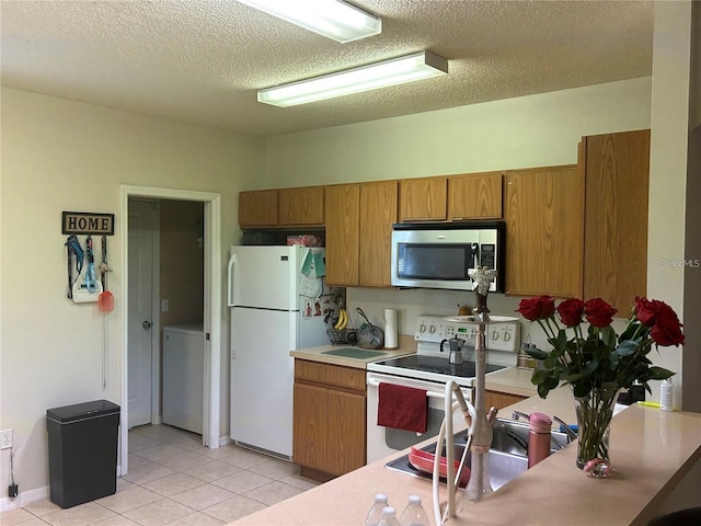 kitchen featuring light tile patterned flooring, a textured ceiling, white appliances, and washer / clothes dryer