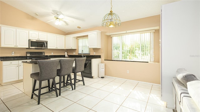 kitchen featuring appliances with stainless steel finishes, a kitchen island, ceiling fan with notable chandelier, white cabinetry, and vaulted ceiling