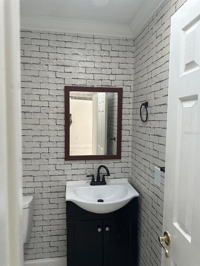 bathroom with vanity, crown molding, toilet, and brick wall