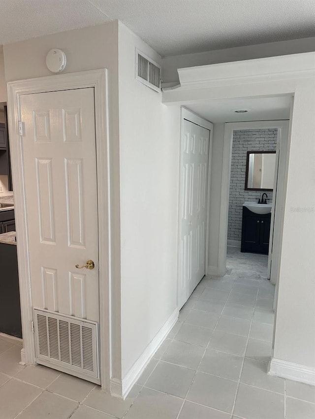 hall featuring a textured ceiling, light tile patterned flooring, and sink