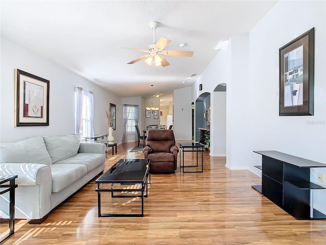 living room featuring lofted ceiling, ceiling fan with notable chandelier, and light hardwood / wood-style floors