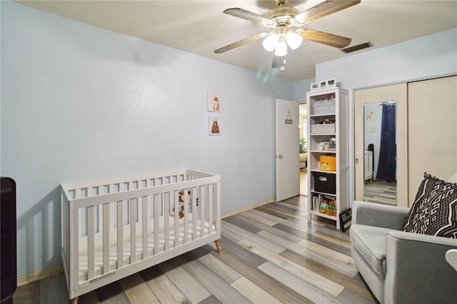 bedroom with a closet, a nursery area, wood-type flooring, and ceiling fan