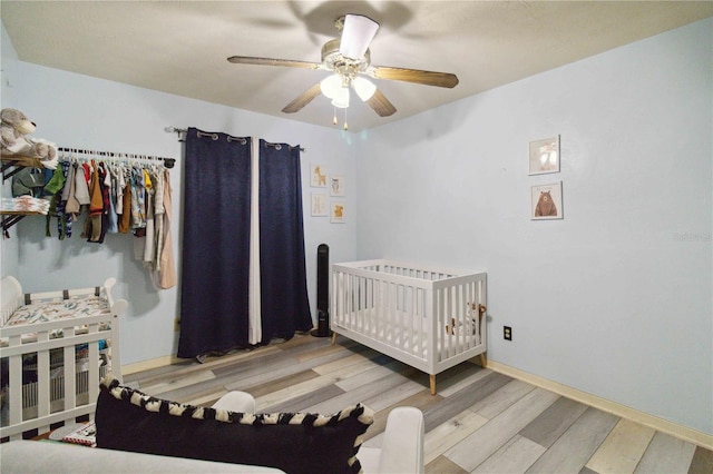 bedroom featuring ceiling fan, light hardwood / wood-style flooring, and a nursery area